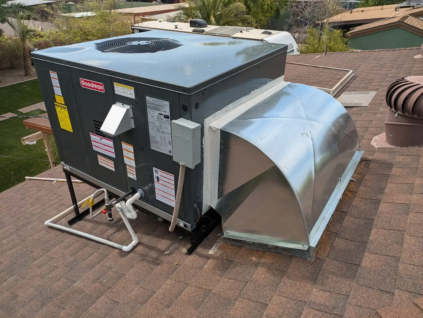 A rooftop HVAC unit with attached ductwork on a shingled roof.