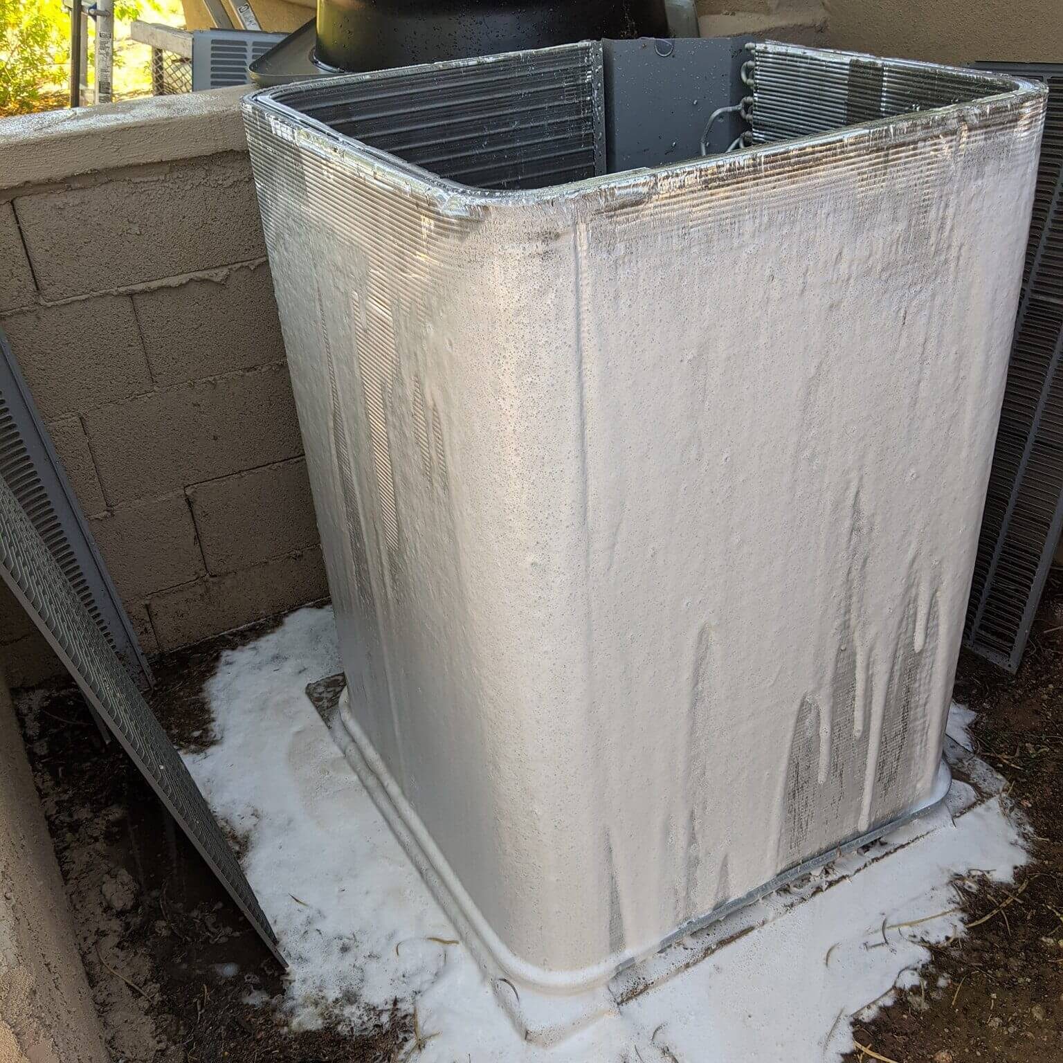 A large outdoor air conditioning unit with foam insulation applied on its base and sides.